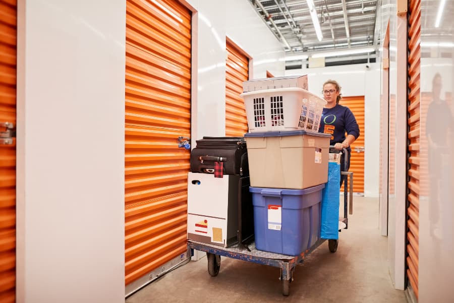 Person pushing trolley full of goods through aisle of self-storage unit building